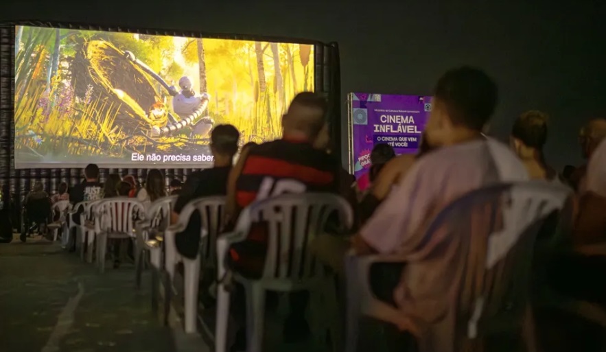 Pessoas assistindo filme em telão inflável ao ar livre em Maricá